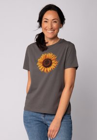 Grijze t-shirt met korte mouwen met een zonnebloemafbeelding met gele bloemblaadjes en een donkere kern, gemaakt van zachte katoen.