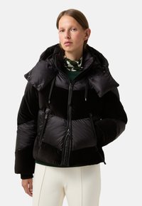 Sort pufferjakke med høj krave og to forskellige stofteksturer. Har lynlåslommer og en cropped pasform. Letvægts- og isoleret design.