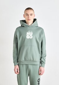 Sudadera verde menta con un bolsillo frontal, capucha ajustable con cordón y logo "HUGO" en blanco. Combinada con pantalones a juego. Mezcla de algodón suave.