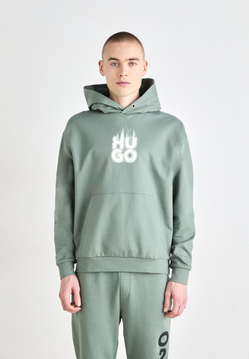 Sudadera verde menta con un bolsillo frontal, capucha ajustable con cordón y logo "HUGO" en blanco. Combinada con pantalones a juego. Mezcla de algodón suave.