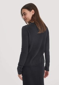 Schwarzer gestrickter Pullover mit langen Ärmeln, rundem Ausschnitt, weicher Textur und figurbetontem Design. Das Model ist von hinten zu sehen.