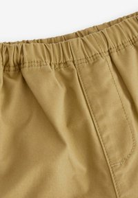 Tissu beige clair avec une taille froncée, dont les coutures sont visibles et qui présente une poche latérale. Texture lisse avec un minimum de détails.