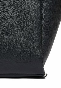 Sac en cuir noir avec une surface texturée, présentant un logo embossé subtil et une forme élégante et épurée.