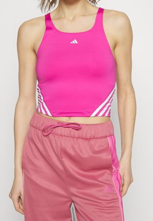 Vrouw draagt een felroze, mouwloos sportief crop-top met witte strepen en roze sweatpants met trekkoord.