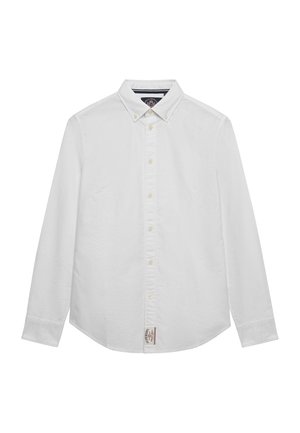 Hvid skjorte med lange ærmer, knappelukning og knappet flipkrave samt et lille stofmærke nederst foran i midten.