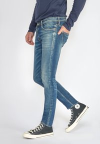 Slim-fit blauwe denim jeans met een vervaagde afwerking, vijf zakken, subtiele stiksels en een gemiddelde taille, gecombineerd met zwarte hoge sneakers.