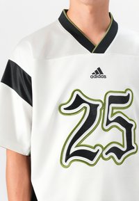White sports jersey featuring a black collar, black shoulder stripes, and large, embroidered number 25 in black and green accents. Adidas logo visible.