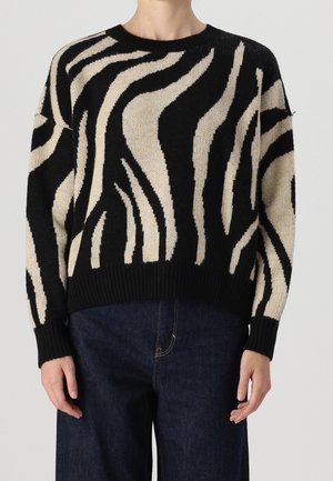 Schwarz-beigefarbener Pullover mit Zebramuster, gestrickt, mit gerippten Bündchen und Saum, kombiniert mit dunkelblauen Jeans.