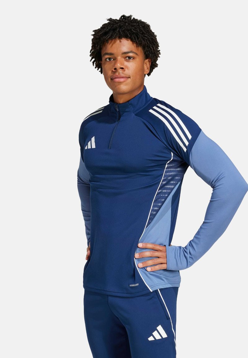Marineblauw sportshirt met halve rits, lange mouwen en drie witte strepen op de schouders. Bevat lichtblauwe zijkanten met textuur.
