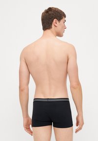 Boxer aderenti neri con un design a vestibilità, caratterizzati da un tessuto liscio e un elastico a strisce in vita. Vista dal retro.