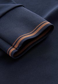 Tessuto atletico blu navy con texture a costine, caratterizzato da un ripiegamento al polsino e due strisce di rame a contrasto vicino ai bordi.