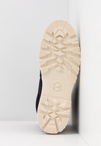 Zapatilla negra con una parte superior texturizada y duradera y una suela de goma beige resistente que presenta un patrón de banda de rodadura multidireccional.