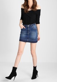 Černý top bez ramínek s přiléhavým střihem a denimová mini sukně s tmavým praním, kontrastním prošíváním a rovný lem.