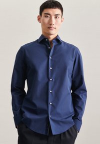 Navy blauwe button-up shirt gemaakt van gladde katoenstof met lange mouwen, een spitse kraag en glanzende witte knopen langs de voorkant.