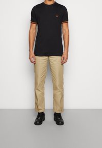 Black t-shirt with orange and red striped sleeves, paired with khaki pants and black shoes. Simple design with a small logo on the chest.