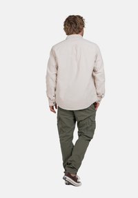 Beige Hemd mit Knöpfen und olivgrüne Cargo-Hosen mit Seitentaschen, kombiniert mit braunen Sneakers. Verfügt über lange Ärmel und eine lockere Passform.