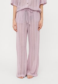 Conjunto de dos piezas de punto en lavanda claro, que presenta una blusa suelta con botones y pantalones con cordón. El material tiene una textura de tejido abierto.
