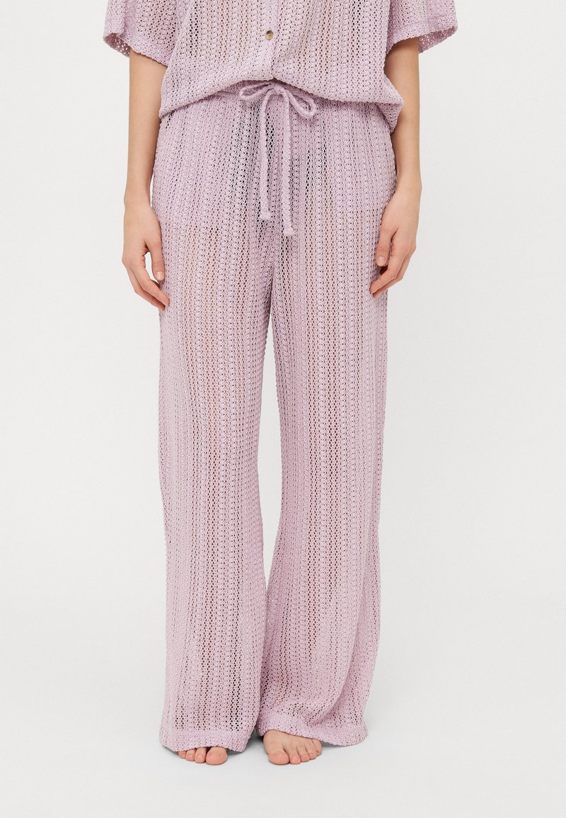 Conjunto de dos piezas de punto en lavanda claro, que presenta una blusa suelta con botones y pantalones con cordón. El material tiene una textura de tejido abierto.