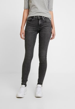 Vaqueros negros ajustados de mezclilla, con un diseño clásico de cinco bolsillos y detalles sutiles de costura. Combinados con una camiseta gris y zapatillas blancas.