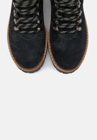 Stivali neri in suede con suola in gomma, dotati di lacci bianchi e neri a fantasia, occhielli in metallo e un bordo cucito marrone.