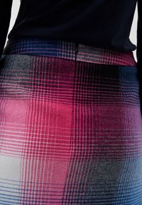 Gros plan d'une personne portant une jupe à carreaux rose, noire, bleue et blanche avec un haut noir rentré à la taille.
