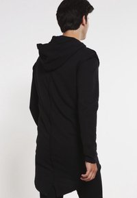 Sudadera con capucha negra, de espalda larga, textura suave y diseño minimalista. Presenta un corte holgado y sin hardware visible.