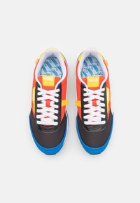 Puma Sneaker mit einer Mischung aus roten, schwarzen und blauen Materialien. Schnürdesign, Gummisohle und eine gemusterte blaue Einlegesohle. Helle Akzente.