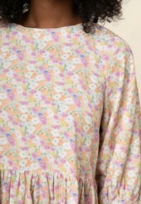 Robe fleurie avec une palette de couleurs pastel comprenant du rose, de l'orange et du violet. Confectionnée dans un tissu doux, elle possède un ourlet à volants et une coupe ample.