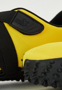 Sport shoes with a vibrant yellow mesh upper, black strap, and textured rubber outsole featuring prominent spikes for traction.