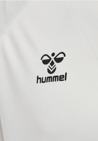 Sort stiliseret bi-logo med teksten "hummel" nedenunder på en glat hvid stofbaggrund.