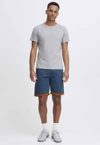 Grå t-skjorte med korte ermer kombinert med marineblå shorts med brune oppbrett. Modellen har på seg grå joggesko og hvite ankelsokker.
