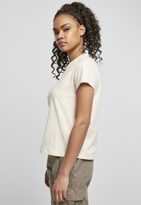 T-shirt a maniche corte di colore crema in cotone, con taglio dritto e scollo rotondo, abbinato a pantaloni cargo verde oliva dotati di tasche laterali.