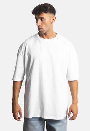 White cotton t-shirt with a loose fit, short sleeves, and a round neckline. Smooth texture and minimal design, worn with light denim pants.