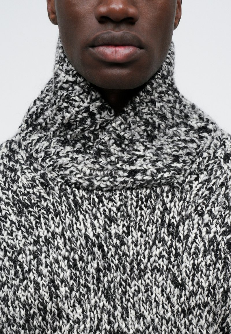 Maglione a collo alto lavorato a maglia in bianco e nero, caratterizzato da un design spesso e testurizzato con un colletto a spirale e una trama di filati misti.