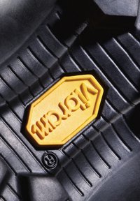La semelle en caoutchouc noir présente un logo "Vibram" jaune bien visible en forme octogonale, avec des rainures texturées pour une meilleure adhérence.