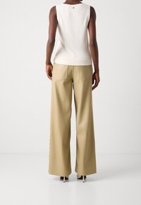 Top senza maniche di colore crema con orlo a coste abbinato a pantaloni beige a gamba larga con tasche posteriori e dettagli di bottone laterali.