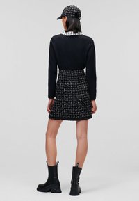 Abito nero a maniche lunghe con gonna in tweed bianco e nero testurizzato e colletto bianco a volant. Abbinato a stivali neri alla caviglia e un cappello abbinato.