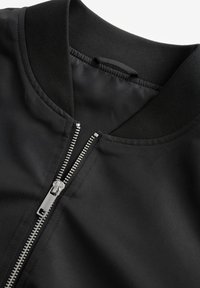 Giubbotto bomber nero con colletto a coste, dotato di una zip in metallo argentato e una finitura liscia e opaca. Dettaglio sul colletto visibile.