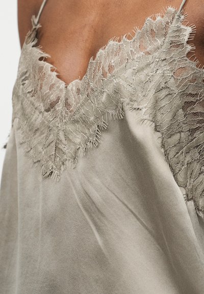 Μπεζ σατέν καμιζόλ με λεπτή δαντέλα στο ντεκολτέ και λεπτές ράντες στους ώμους, σε άτομο με μεσαίο τόνο δέρματος.