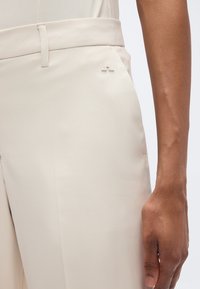 Μπεζ παντελόνι με απαλό, ραμμένο ύφασμα. Διαθέτει πλαϊνή τσέπη και διακριτικό ανάγλυφο λογότυπο. Σχεδιασμός με ίσια μπατζάκια και καθαρές γραμμές.