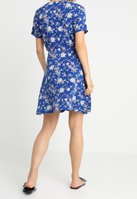 Sininen lyhythihainen mekko kukkakuviolla, jossa on tiukka vyötärö ja levenevä hame. Sileä kangas ja polvipituinen malli.