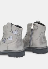 Botas tobilleras grises con recortes en forma de corazón brillantes, acabado texturizado, cremallera lateral y una suela negra de goma resistente. Diseño funcional y detalles llamativos.