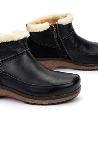 Botas de cuero negro hasta el tobillo con un forro de crema suave, cremallera lateral y suela texturizada marrón, con punta redondeada y acabado suave.