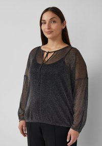 Schwarze transparente Bluse mit langen Ärmeln, rundem Ausschnitt und Kordelzug-Detail. Strukturierter Stoff mit subtiler Schimmerung und gepunkteten Akzenten.