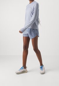 Světlomodré sportovní tričko s dlouhým rukávem v kombinaci s odpovídajícími modrými šortkami. Neformální tenisky mají šedé a modré akcenty, jsou navrženy pro pohodlí.