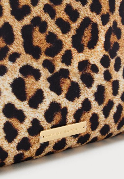 Pogled od blizu na tkanino z leopardjim vzorcem z zlato označbo Loeffler Randall, pritrjeno blizu spodnjega roba.