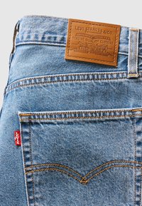 Lichtblauwe denim jeans met een tan leren label met verhoogde branding. Bevat een rode tab en gouden stiksels op de zakken.
