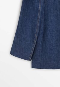 Sininen farkkukangas, jossa on näkyvä sivusauma, jossa on kontrastiväristä kultalankaa ja siisti leikattu reuna. Silkkinen pinta, rento muotoilu.