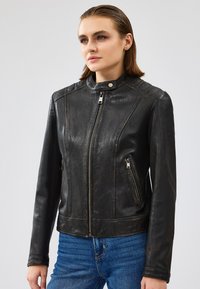 Giacca da motociclista in pelle nera con un design aderente, colletto alto e chiusure con zip. Presenta dettagli imbottiti sulle spalle e tasche laterali.