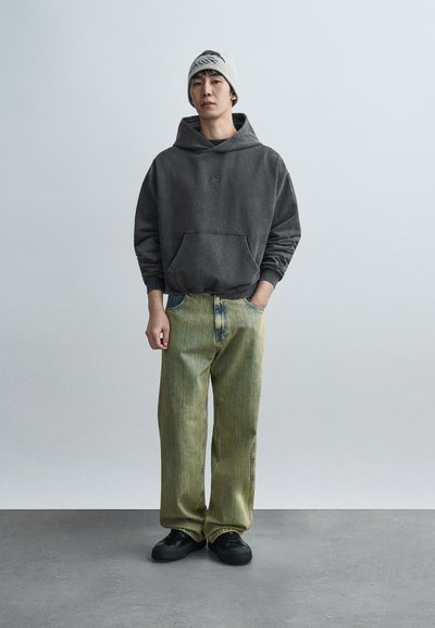 Γκρι φούτερ με κουκούλα και μπροστινή τσέπη, σε συνδυασμό με παντελόνι φαρδύ με κίτρινα-πράσινα ρίγες. Μαύρα παπούτσια ολοκληρώνουν το ντύσιμο. Απλό, καθημερινό στυλ.